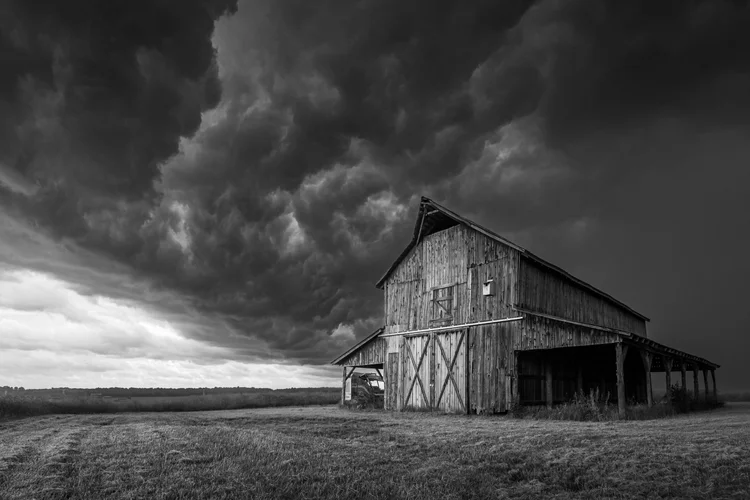 Black-and-white photograph of a barn beneath dramatic storm clouds